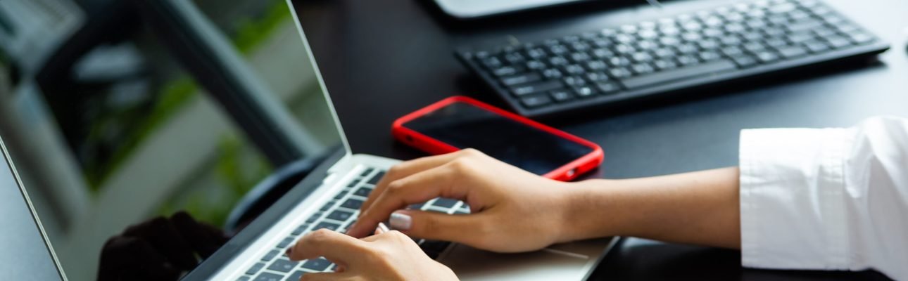 Close up hand of female typing on keyboard of laptop on table, working with technology device in modern office