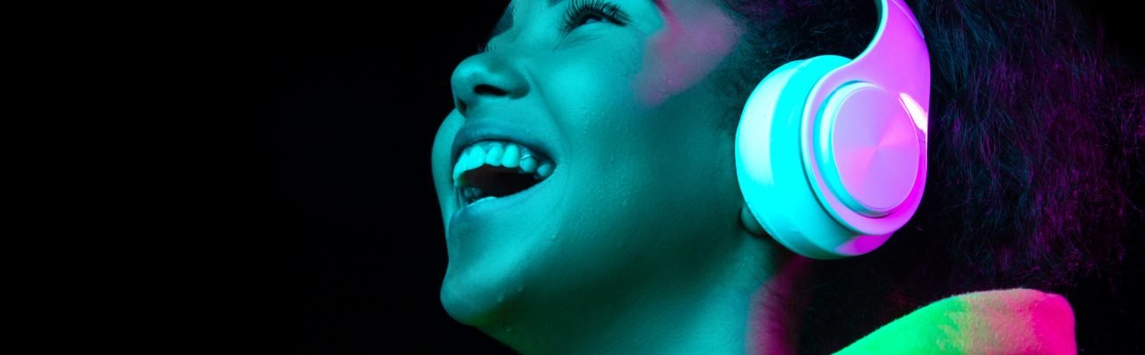 Headphones. African-american woman's portrait isolated on dark studio background in multicolored neon light. Beautiful female model. Concept of human emotions, facial expression, sales, ad, fashion.